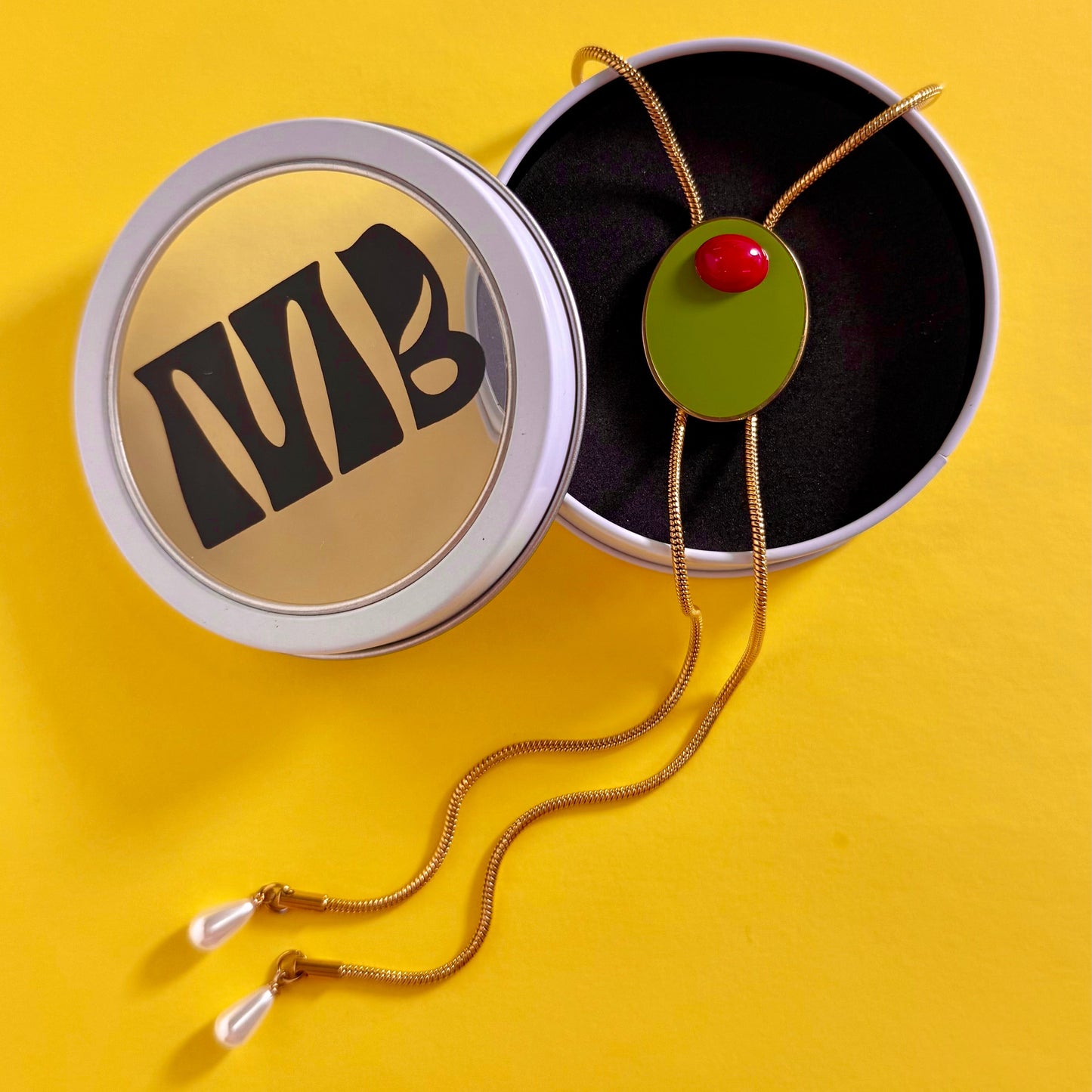 Olive Bolo Necklace with a green pendant and red stone on a yellow background in a MackBecks custom white window tin