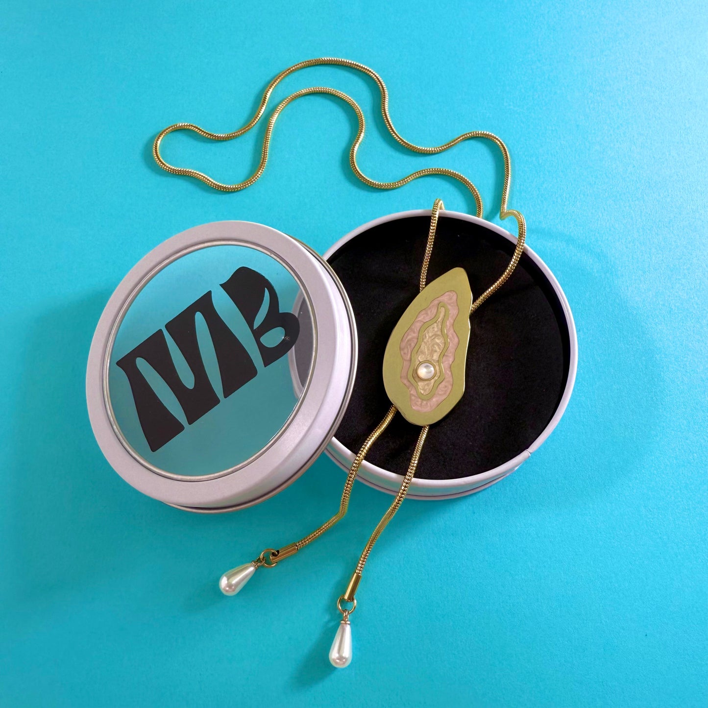 MackBecks Gold-Plate Oyster Bolo on teal background in white MackBecks branded circle window tin.