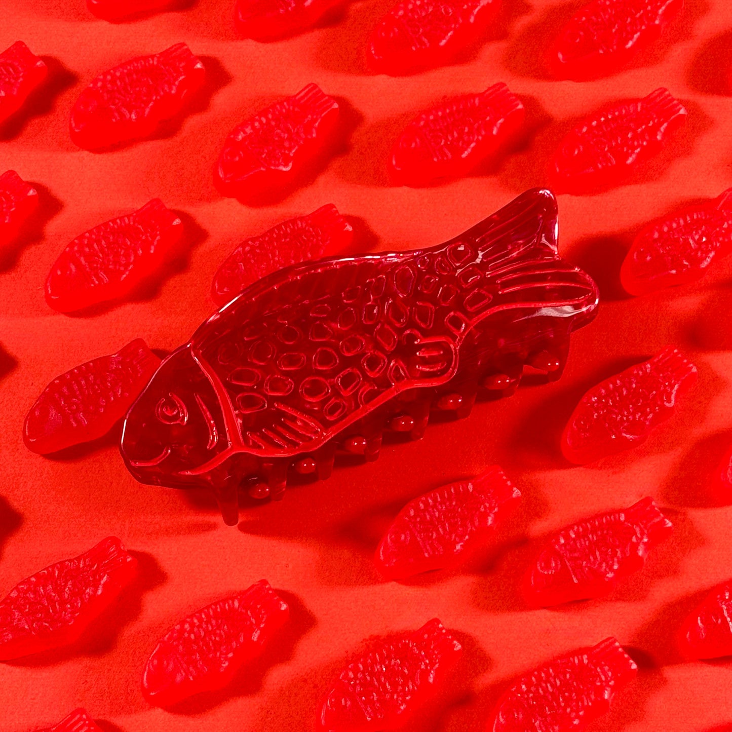Red fish-shaped gummy candies with a red sweetish fish hair claw on a red background