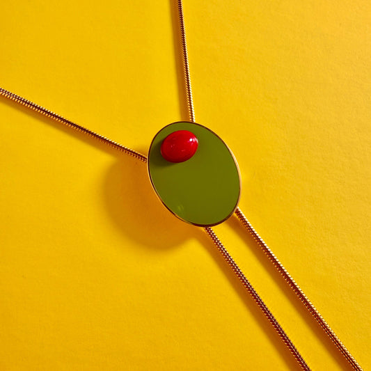 Olive Bolo Necklace with a green pendant and red stone on a yellow background