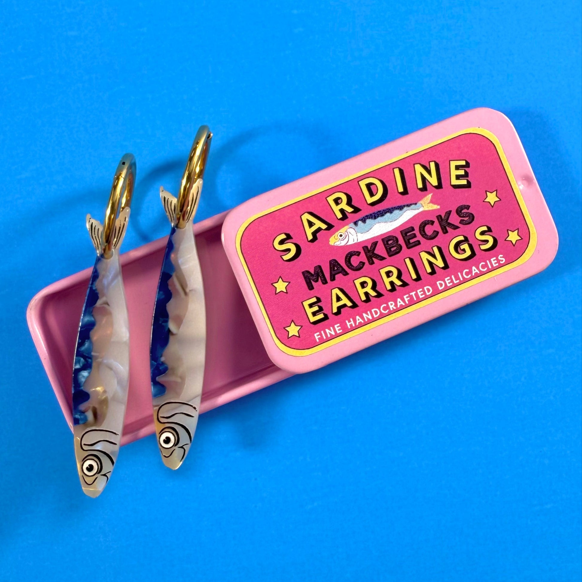 MackBecks Original Sardine Earrings in a Pink Retro Tin on a blue background.